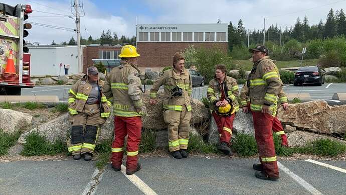 Tired and dirty firefighters are seen suited up standing in a circle in a parking lot.