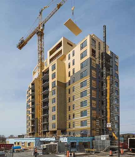 A photo shows a high-rise mass-timber building under construction, with a crane lowering a large wooden panel into place atop the structure.