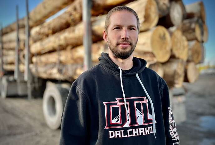 A man with a beard in front of a logging truck.