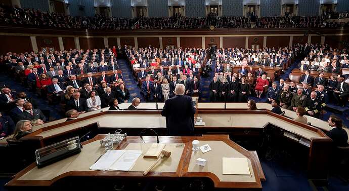 Donald Trump is seen from behind as he stands looking toward the audience in the House chamber.