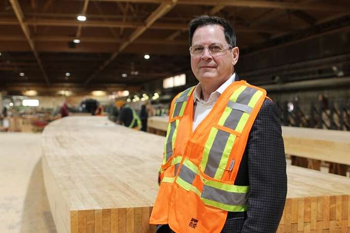 A man wearing safety glasses and a safety vest is pictured in front of a large beam made of glue-laminated timber.