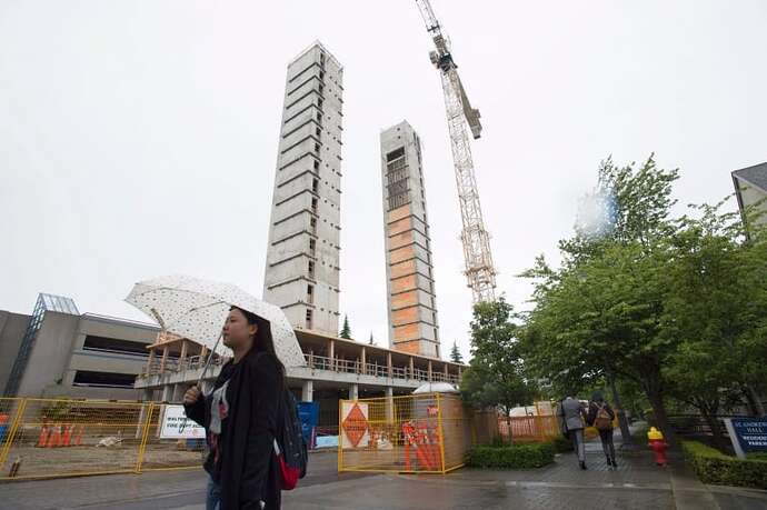 A woman with an umbrella walks past a construction site for two tower structures with a crane on an overcast day in Vancouver, B.C.