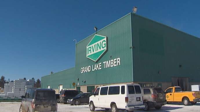 The outside of a green-cladded industrial building with a large Irving corporate logo sign on the front, with "grand lake timber" in green letters below it. Several vehicles are parked in the yard around the building.