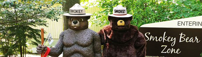 A person wearing a Smokey Bear costume standing next to a statue of Smokey Bear near a sign that reads "ENTERING Smokey Bear Zone."