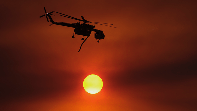 A helicopter flies past the sunset after it dropped water on a wildfire burning behind homes in a hillside Tuesday, Sept. 6, 2022, near Hemet, Calif.