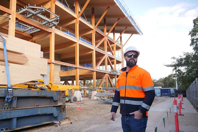 a man in a hardhat stands outside a large timber building