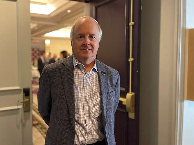 Man with white hair and a suit standing in a doorway.