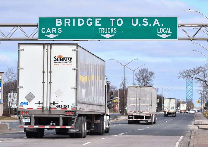 Transport trucks drive under a highway sign reading 'Bridge to U.S.A.'