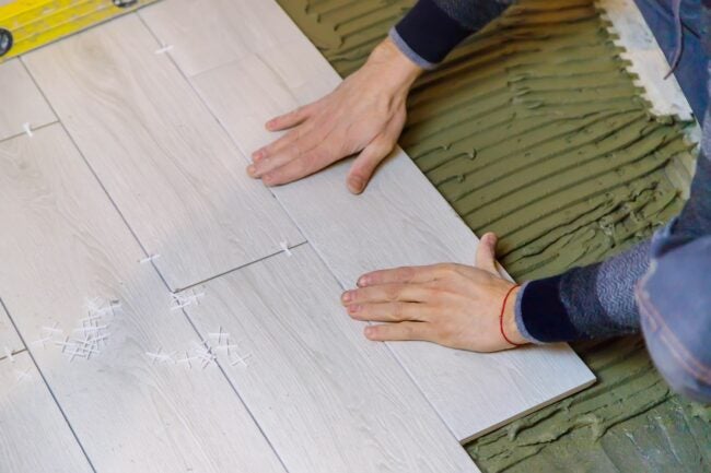 A pair of hands lays down light colored wood floor planks.