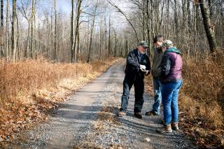 Forest Service foresters and property owners standing on a dirt roadway through a forest looking at and discussing a measurements document.