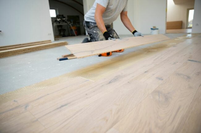 A person is laying down light colored wood floor planks in an unfinished room.
